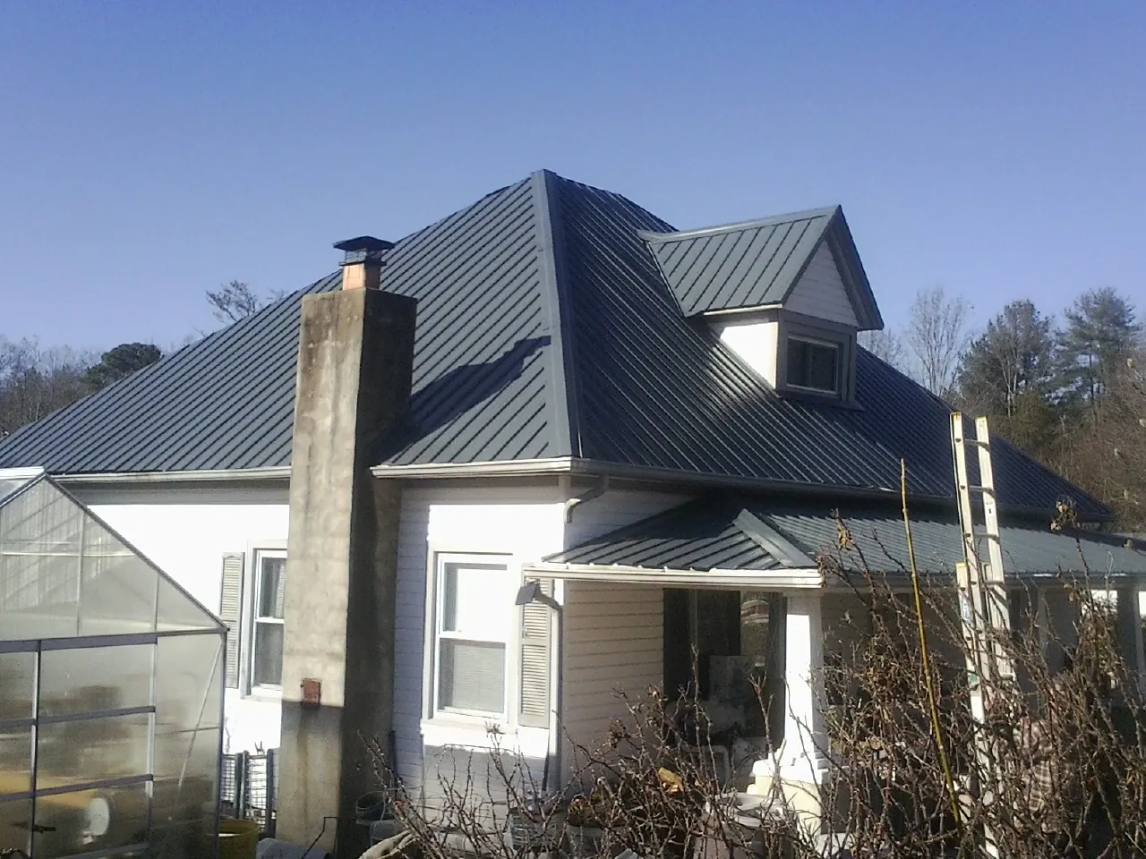 Dark blue standing seam metal roof on a white farmhouse with dormer — Slate & Tile Roof Repair by Roofing Brothers in Fisher