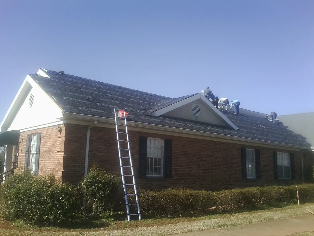 Crew tearing shingles off a brick ranch roof with a ladder set — Emergency Roof Repair work by our crew in Fisher