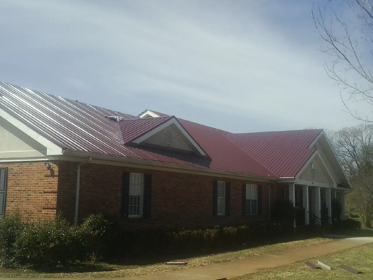 Red metal roof with gabled entries on a long brick building, from a Hail Damage Roof Repair job in Fisher