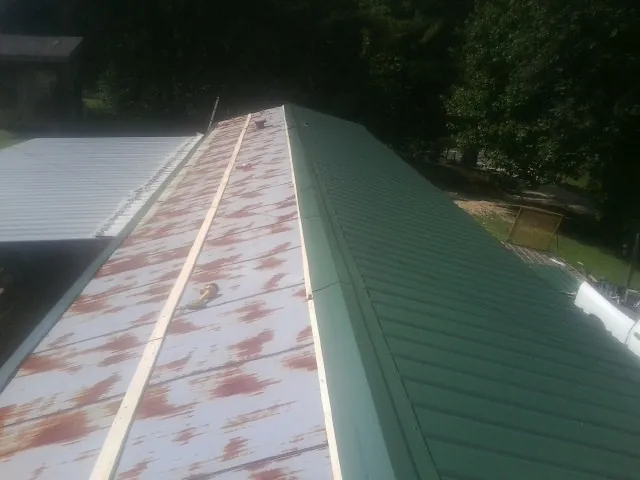 Old rusted panels beside newly installed green metal roofing — Wind Damage Roof Repair by Roofing Brothers in Fisher