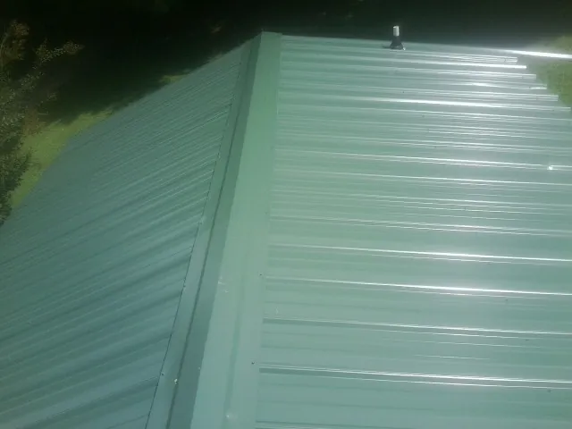New green metal panels meeting at the ridge of a roof — Flat Roof Repair work by our crew in Fisher
