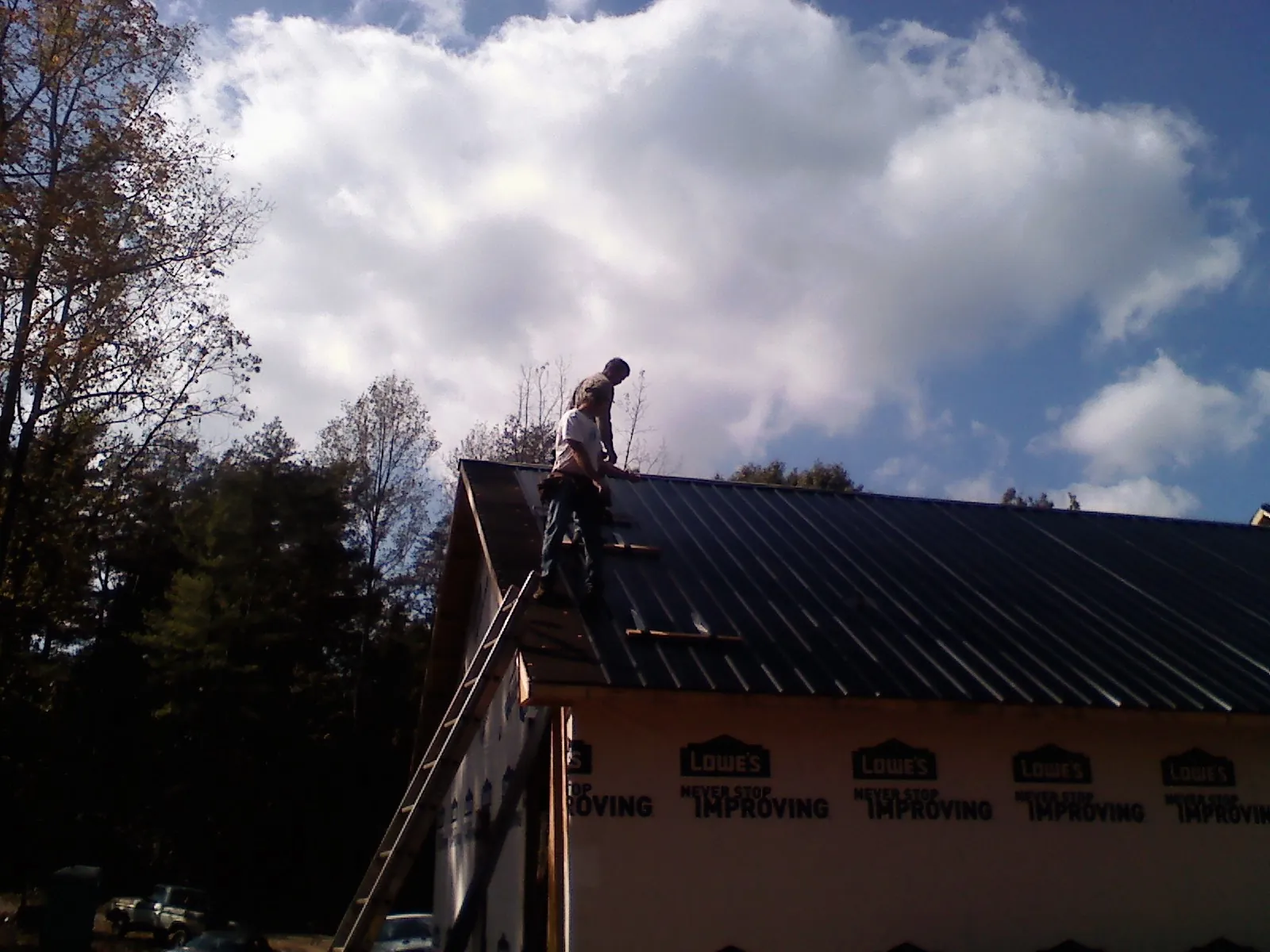 Roofer fastening dark metal panels high against a cloudy sky, from a Roof Inspection job in Fisher
