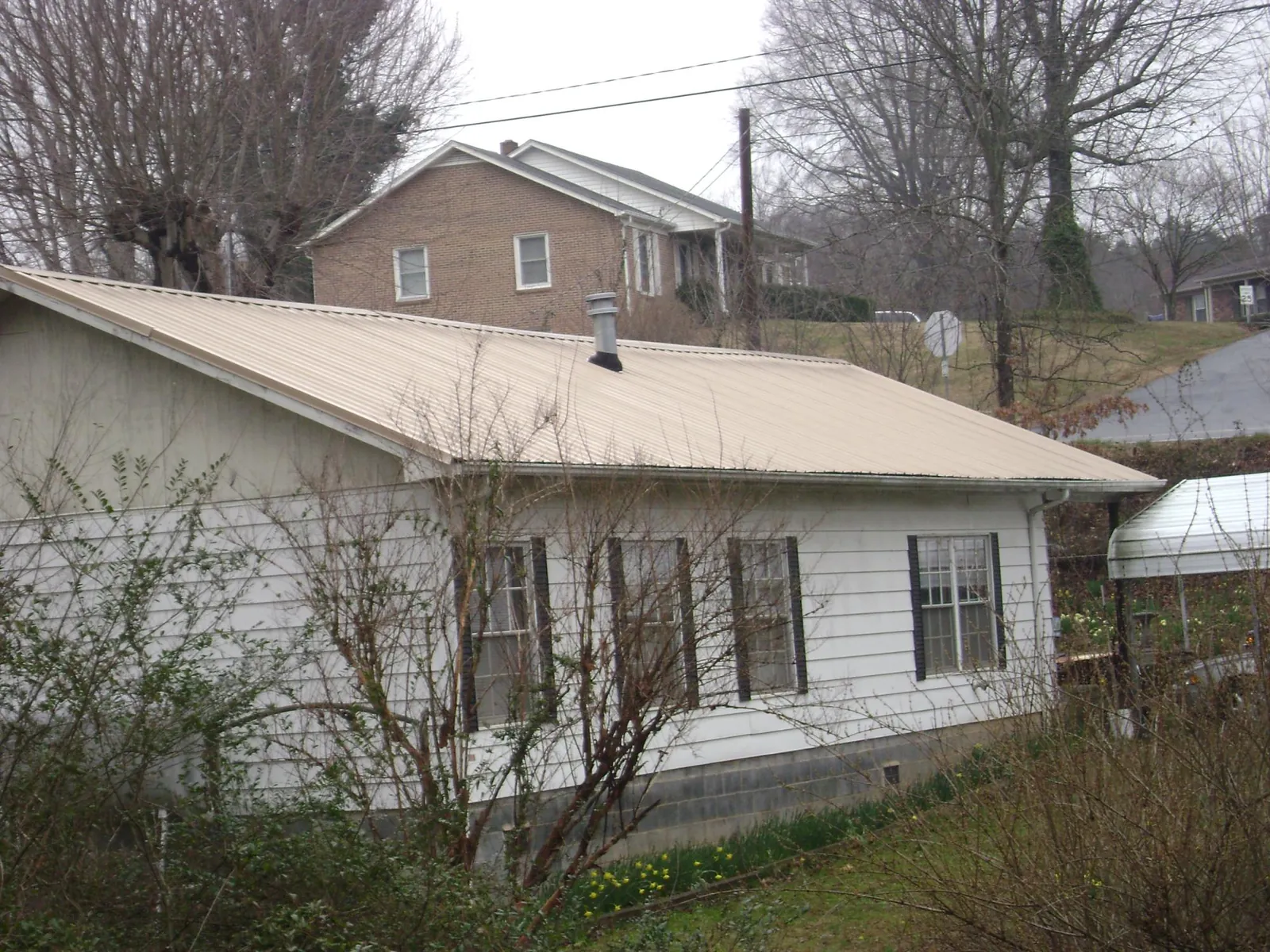 Tan metal roof on a white sided house set into a hillside — Commercial Roofing by Roofing Brothers in Fisher