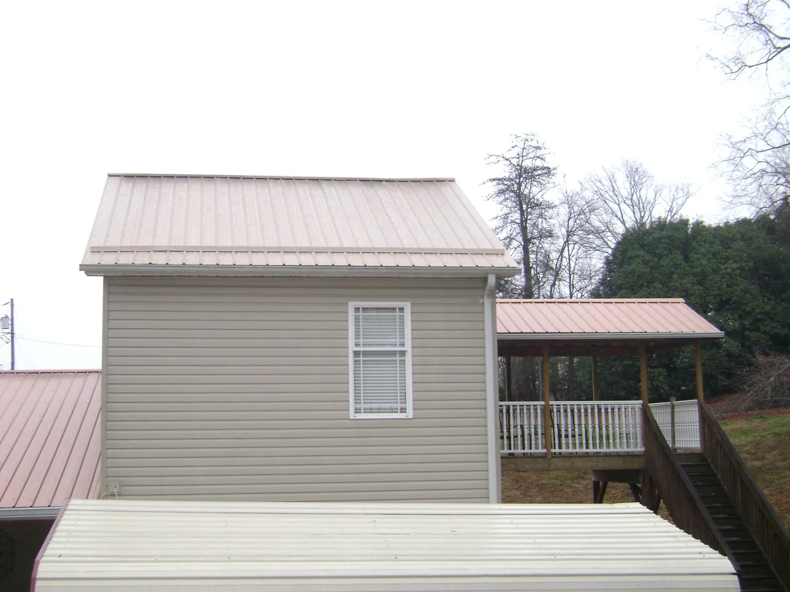 Tan metal roofs on a two story addition and attached porch, from a Roof Replacement job in Fisher
